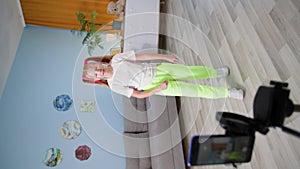 blogger child girl with pink hair waves her hand and speaks in front of mobile phone on tripod, kid dancing for social