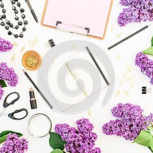 Blogger or freelancer workspace with clipboard, notebook, lipstick, branches of lilac and accessories on white background. Flat la