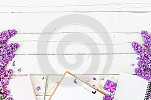 Blogger or freelancer workspace with clipboard, notebook, pen, lilac, box and petals on wooden background. Flat lay, top view. Bea