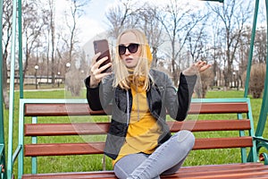 The blogger girl sits on a swing in the park and creates content. Work in social networks, video blogging and photo blogs. The