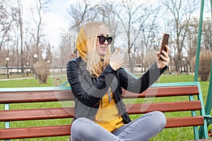 The blogger girl sits on a swing in the park and creates content. Work in social networks, video blogging and photo blogs. The