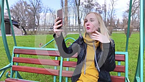The blogger girl sits on a swing in the park and creates content. Work in social networks, video blogging and photo blogs. The con