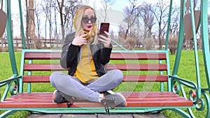 The blogger girl sits on a swing in the park and creates content. Work in social networks, video blogging and photo blogs. The con