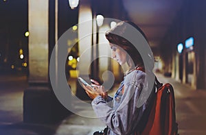 Blogger hipster using in hands gadget mobile phone, woman with backpack pointing finger on blank screen smartphone on background b