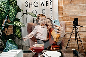 Blogger mother and her little daughter have fun together with the vlog camera. Young parenting blogger recording a video