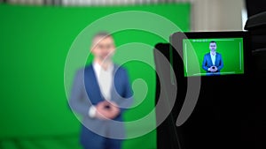 A blogger is recording a video on a green background.  The camcorder is recording a blogger