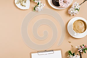 Blogger\'s flat lay. A cup of coffee, donuts, apple blossoms, a tablet on a beige background with a copy space