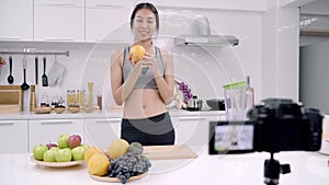 Blogger sporty Asian woman using camera recording how to make orange juice video for her subscriber, female use organic fruit.