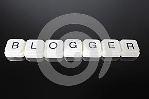 Blogger text word title caption label cover backdrop background. Alphabet letter toy blocks on black reflective background. White