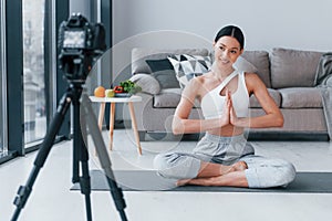 Blogger young woman with slim body shape in sportswear talking about vegetables, fruits and healthy food indoors at home