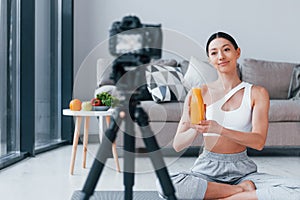 Blogger young woman with slim body shape in sportswear talking about vegetables, fruits and healthy food indoors at home