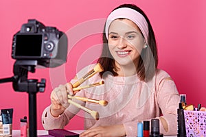 Blogging, modern technology and people concept. Happy smiling woman beauty video blogger holds brushes for makeup while recording photo