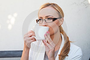 Blon hair girl in glasses and suit sitting on the bench with cu