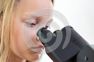 A blond 9 year old schoolchild looks into the eyepiece of a microscope. Isolated