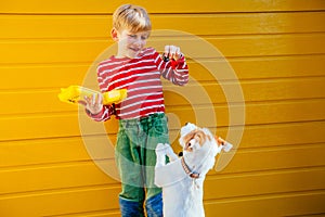 Blond baby boy with lunch box with some food playing, training with his dog