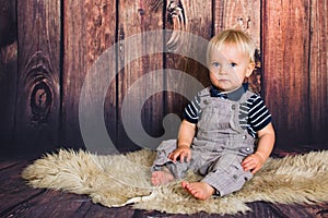 Blond baby sitting in front of wooden background in studio. Child studio photoshot with copy space