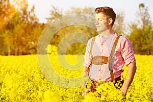Blond bavarian man standing in a field of yellow flowers