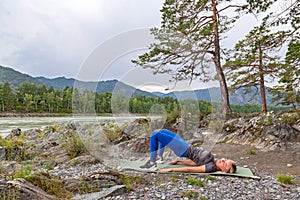 Blond beautiful girl is making a warm-up lying on the stone ground in the pose of the bridge, resting his palms and shoulder