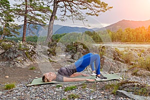 Blond beautiful girl is making a warm-up lying on the stone ground in the pose of the bridge, resting his palms and shoulder