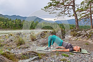 Blond beautiful girl is making a warm-up lying on the stone ground in the pose of the bridge, resting his palms and shoulder