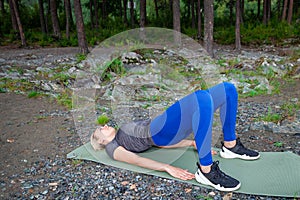 Blond beautiful girl is making a warm-up lying on the stone ground in the pose of the bridge, resting his palms and shoulder