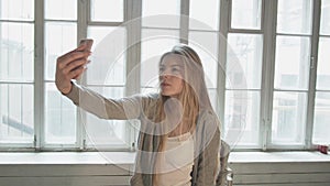 A blond blonde on the opposite window makes selfie using a smartphone. Beautiful young woman is shooting herself at the