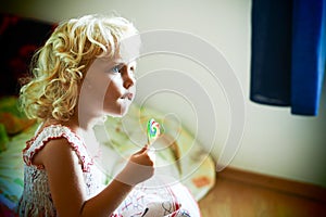 Blond blue eyed baby girl with a candy in her hand