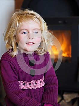 Blond blue eyed little girl sitting in front of a fireplace