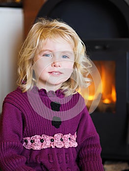 Blond blue eyed little girl sitting in front of a fireplace