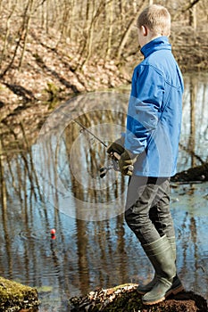 Blond boy in blue jacket and gloves fishing