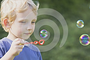 Blond boy in blue shirt blows bubbles