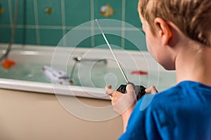 Blond boy with British flag on blue Tshirt playing with radio controled boat in bathroom
