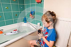 Blond boy with British flag on blue Tshirt playing with radio controled boat in bathroom
