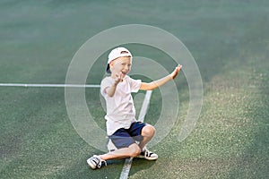 A blond boy in a cap in a sports uniform sits on a soccer ball on the football field and shouts Goal, sports section. Training of