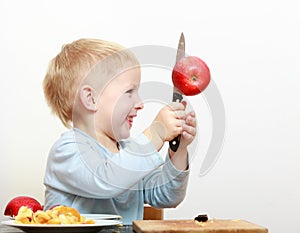 Blond boy child kid preschooler with kitchen knife cutting fruit apple