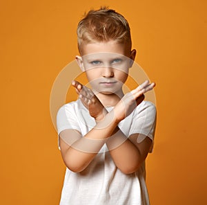 Blond boy child in white t-shirt and jeans standing and showing stop rejection sign by hands looking at camera