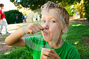 Blond boy eating a commercial yogurt in a park as snack