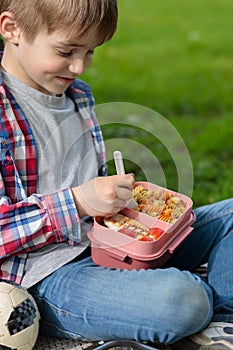 A blond boy eats lunch from a plastic container. Lunch in nature after training, lessons. Selective focus