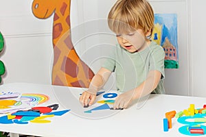 Blond boy form shapes standing by the table in kindergarten