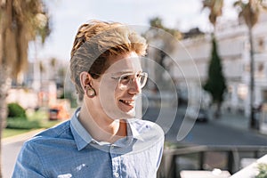 Blond boy with glasses and piercings smiling sitting on a terrace