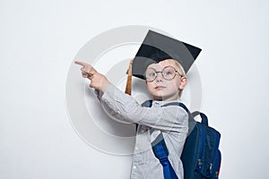 Blond boy in glasses with serious look shows on board. Boy wearing student hat. Kids achievement. Copy space