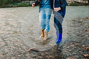 Blond boy in hat and girl playing at river shore. Kids wear rain boots