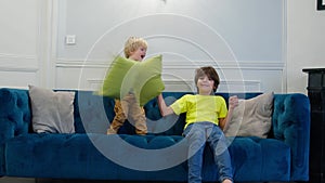 Blond boy and his brother fight with pillows on the coach