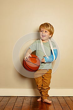 Blond boy hold basketball ball with broken hand in plaster cast