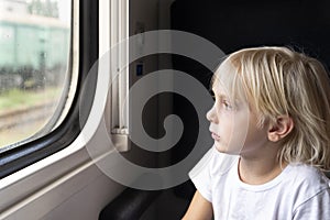 Blond boy looks thoughtfully out the train window. Rail travel