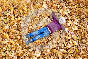 Blond boy in a plaid shirt lies in yellow autumn leaves. Top view. Autumn concept