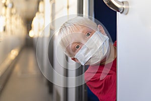 Blond boy in protective mask rides train compartment. Traveling during a quarantine. Empty train