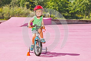 Blond boy ride small bicycle with learning wheels around cones
