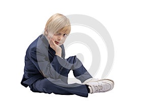 Blond boy in school uniform sits on white background. Portrait of student of the 1st or 2nd grade