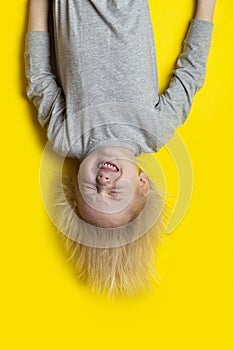 Blond boy upside down on yellow background and grimaces. Vertical frame